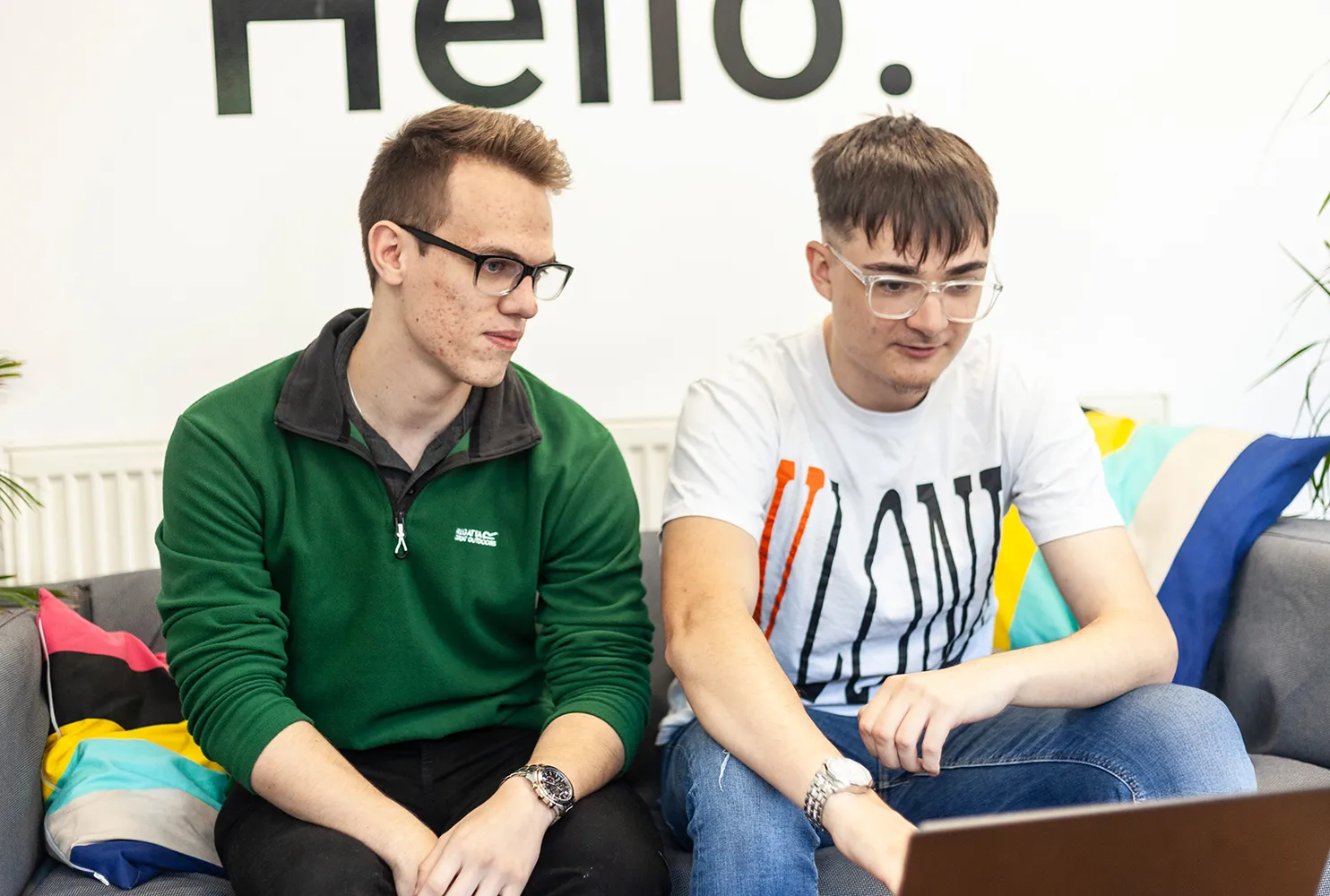 Two men sitting on a colorful sofa, focused on a laptop.