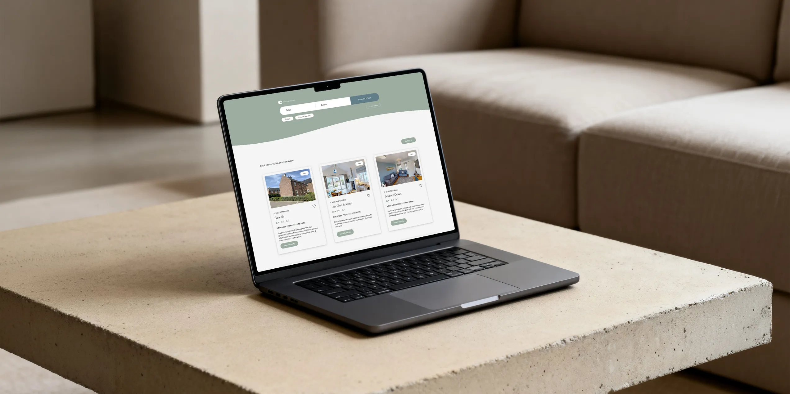 A laptop on a beige coffee table displays the Filey Bay website with property listings.